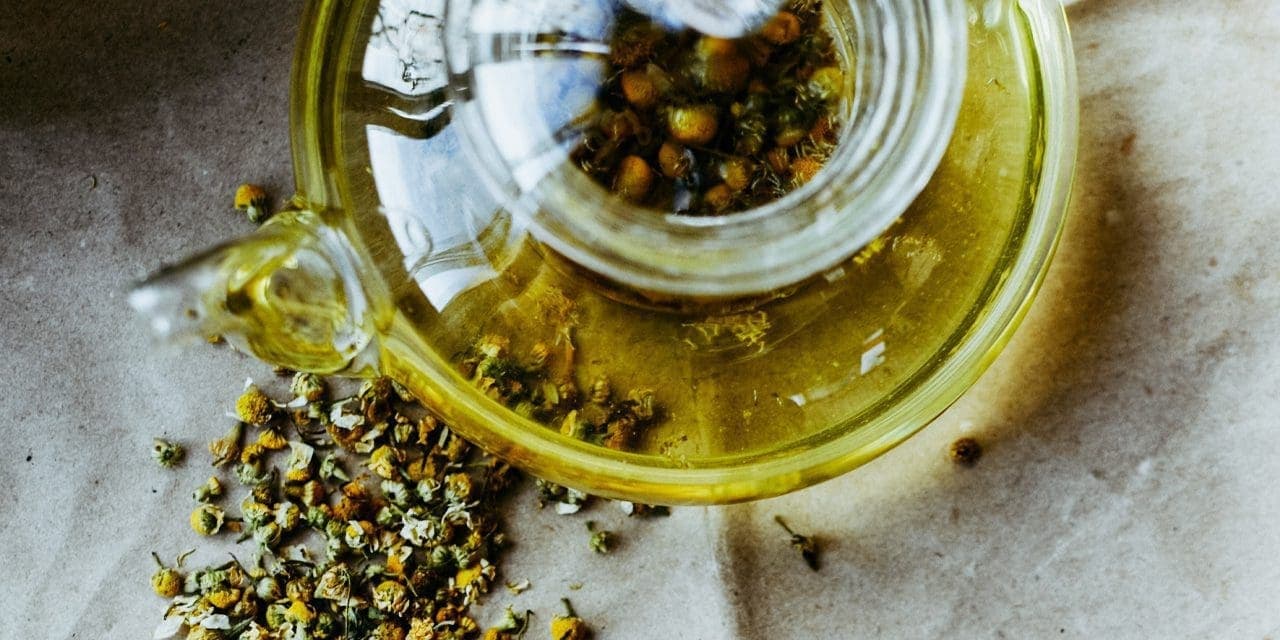 top view of glass teapot with dried chamomile flowers on the outside and inside of the tea pot