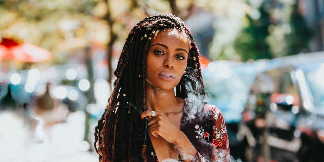 dreadlocks haired black woman holding vape pen under neck